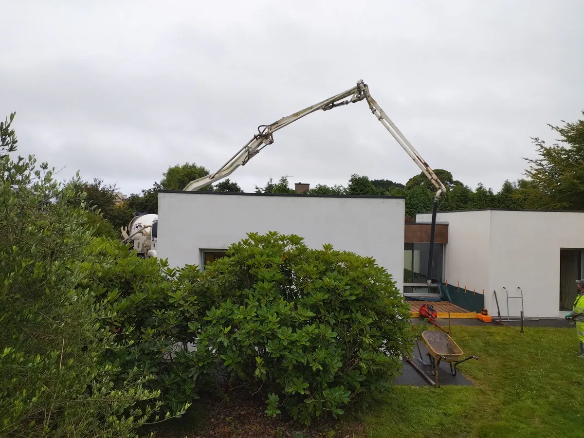 Camion pompe à bras articulé acheminant le béton par-dessus une maison