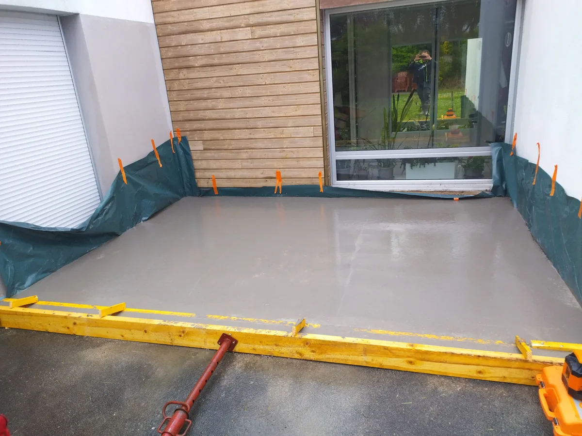 Dalle béton de terrasse fraîchement talochée devant une baie vitrée, bâche de protection agrafée sur le bardage