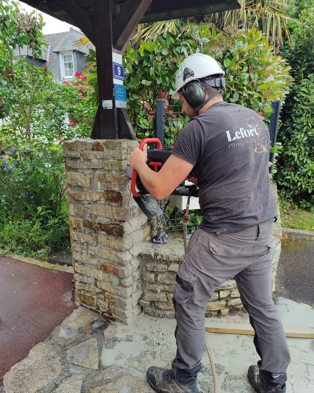 Maçon de LEFORT Maçonnerie découpant un pilier en pierre à la scie à disque, casque et protections auditives