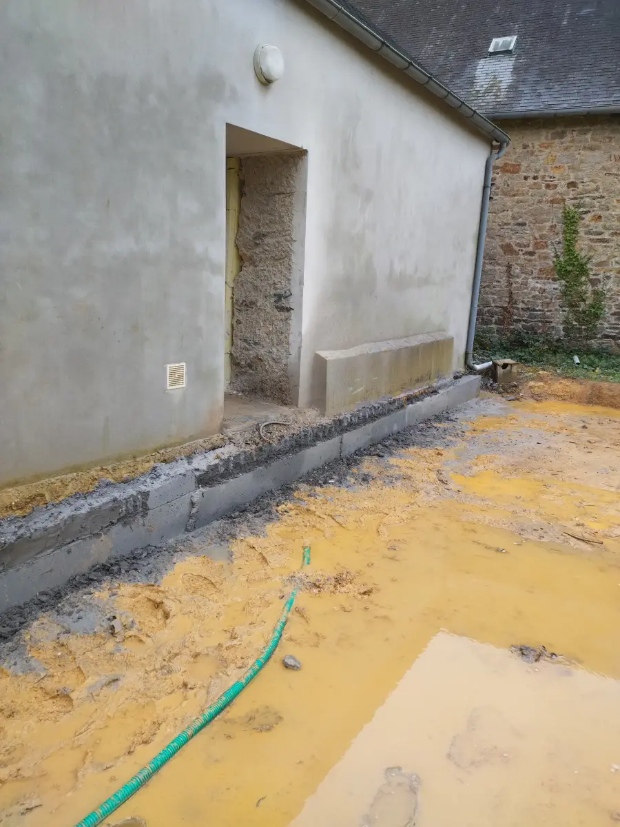 Volume neuf enduit greffé contre un mur en pierre ancien, soubassement et drainage en cours