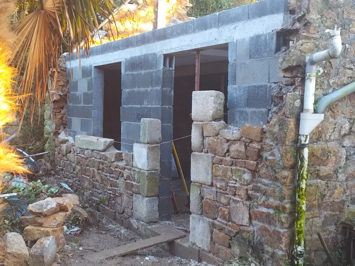 Élévation neuve en parpaing montée sur les murs en pierre existants, linteaux en pierre de taille et planelle béton en tête de mur