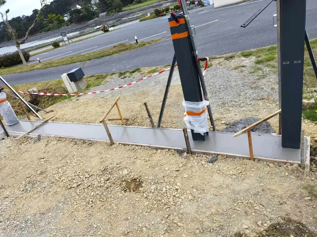Longrine béton coulée dans son coffrage avec poteaux de clôture scellés, chantier en bord de mer