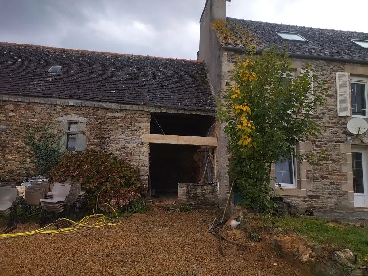 Grande ouverture percée dans le mur en pierre d'un corps de ferme, poutre en place