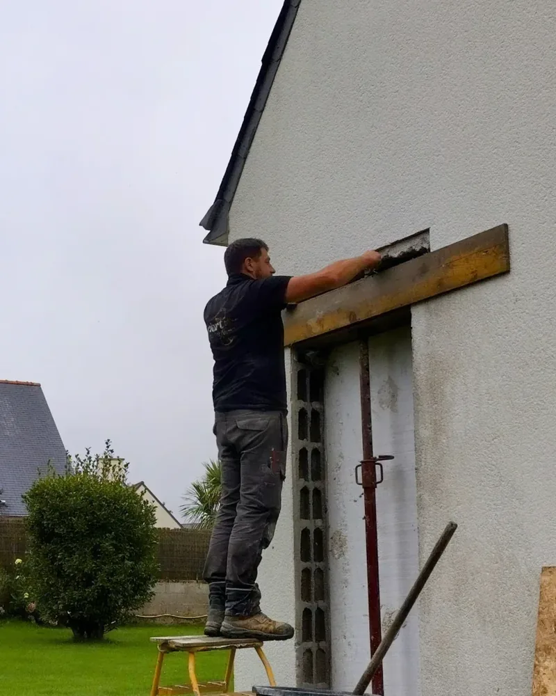 Maçon appliquant le mortier au-dessus de la poutre acier posée dans une ouverture de façade