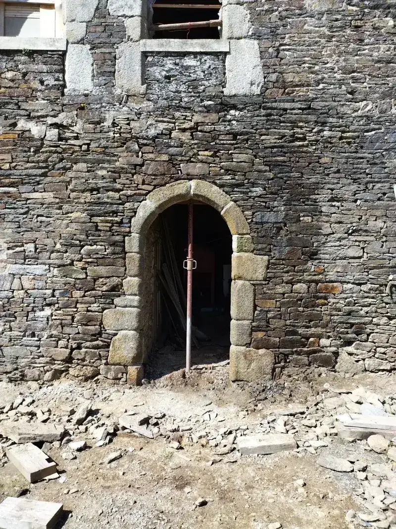 Porte cintrée en pierre de taille dans un mur de schiste, arc et jambages en granit remontés