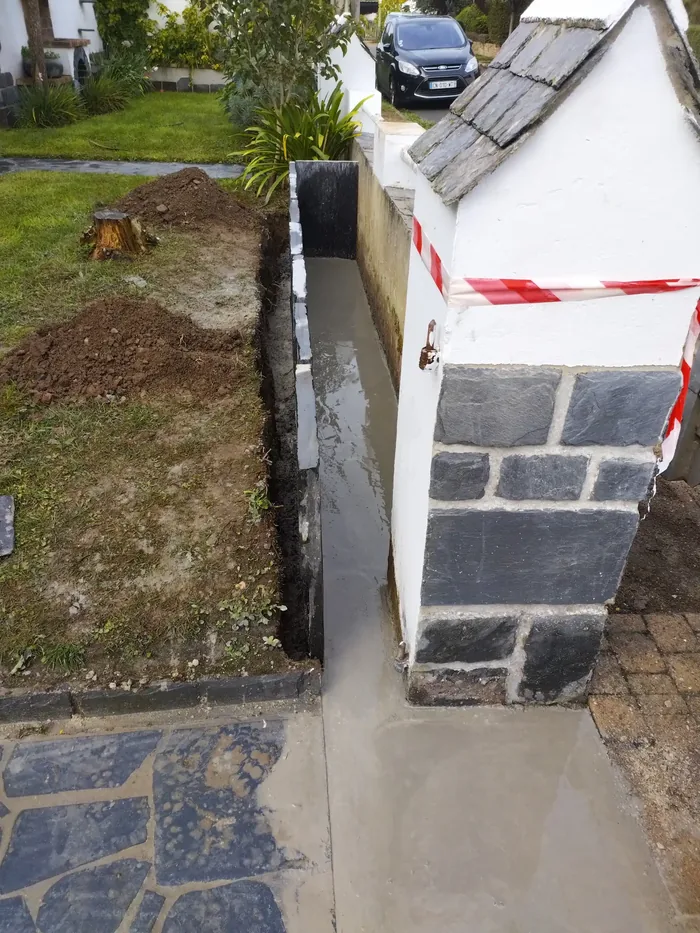 Bande béton coulée entre un pilier en pierre et une allée pavée, balisée au rubalise
