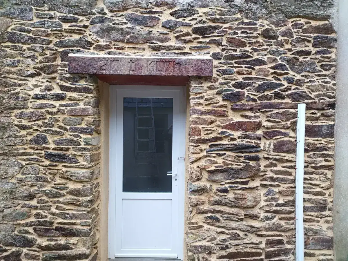 Mur en pierre rejointoyé autour d'une porte, linteau en bois gravé an ti kozh