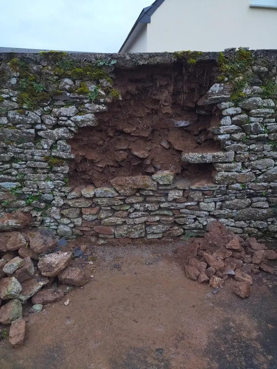 Brèche ouverte dans un mur de clôture en pierre, cœur de terre visible